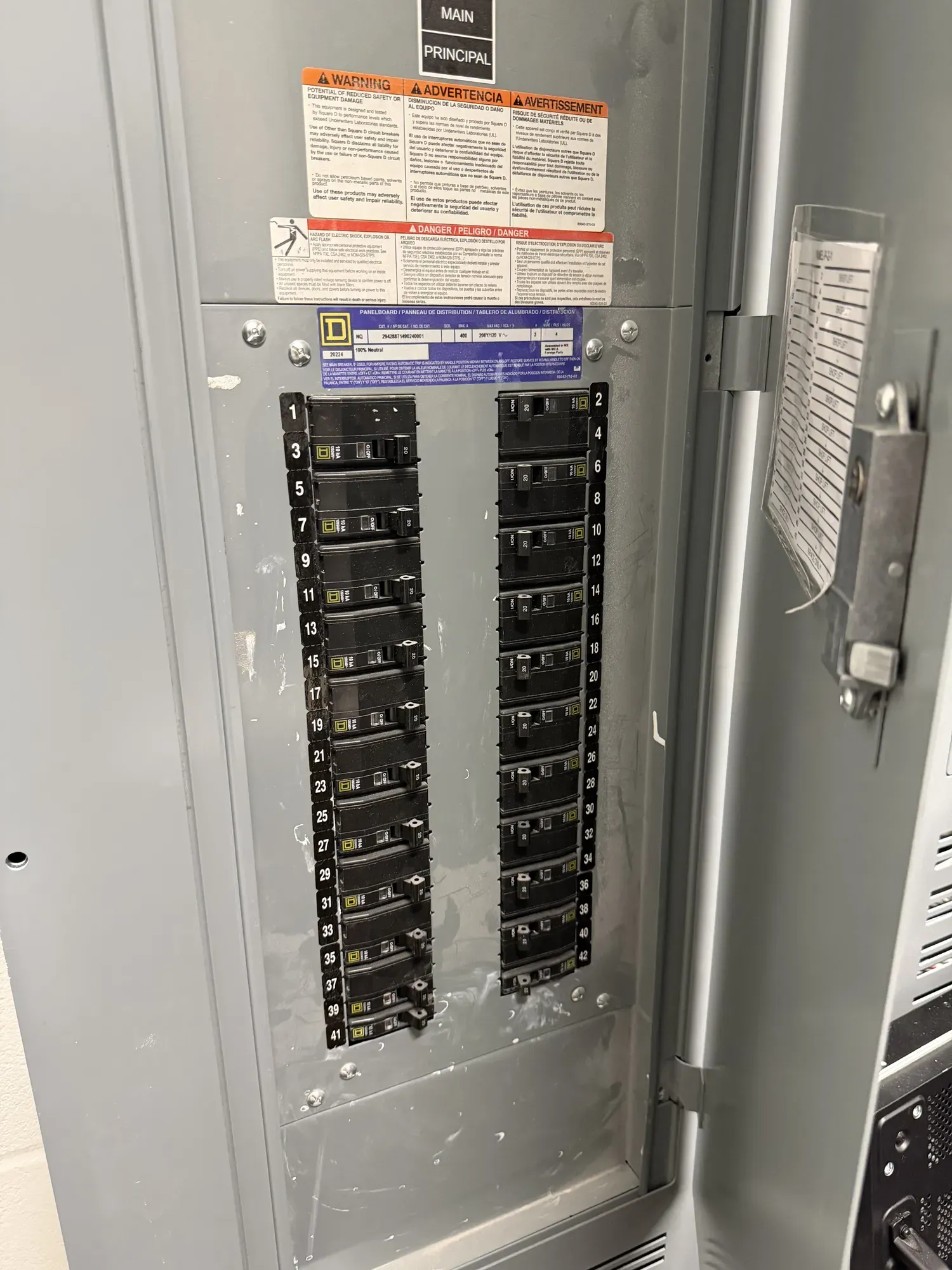 A main electrical panel with its door open, showing two rows of labeled breakers and the manufacturer's warning labels