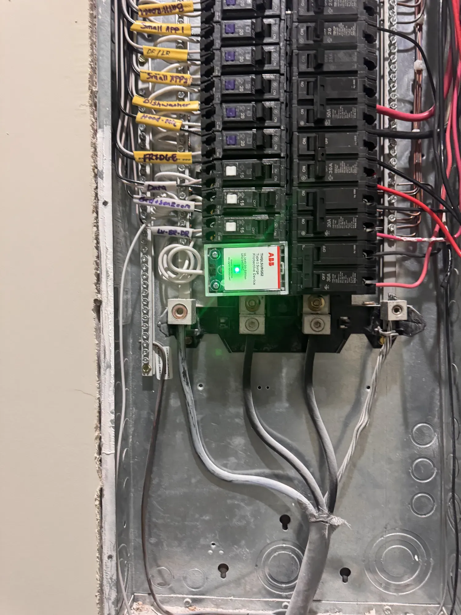 An open electrical panel with labeled breakers and a surge protective device glowing with a green status light at the bottom