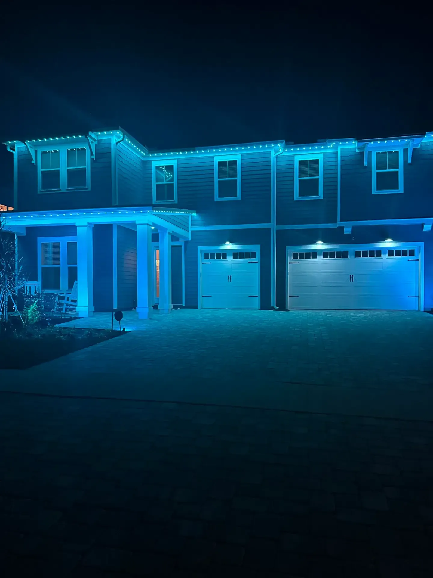 Two-story home lit in teal by Jellyfish permanent lighting at night