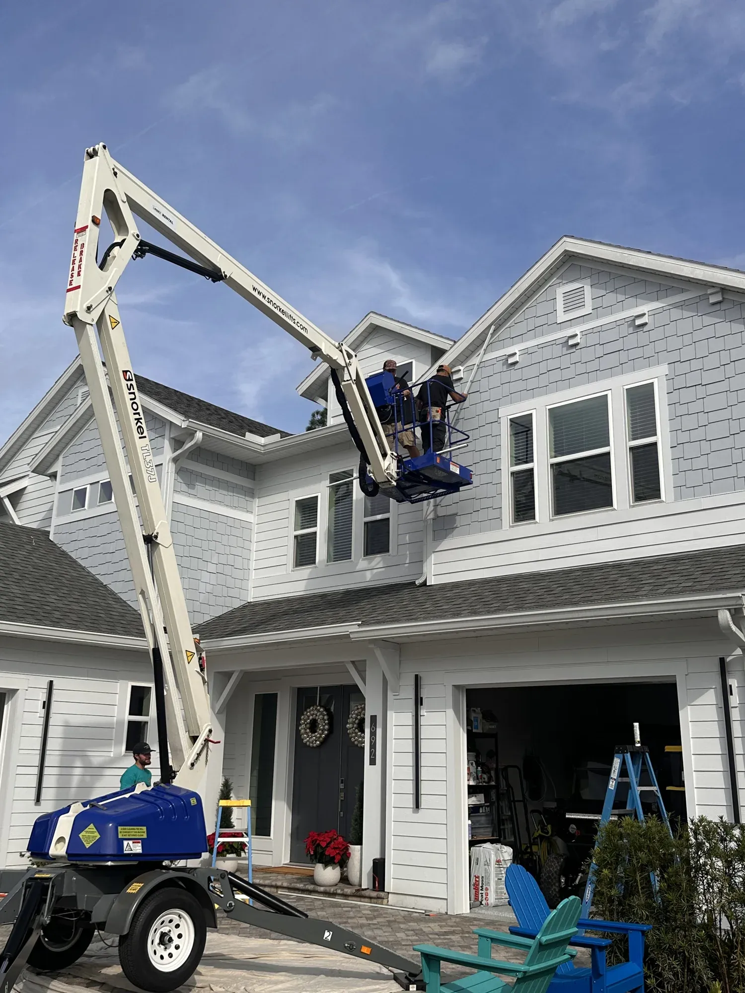 Boom lift raising an electrician to the second story of a new coastal-style home