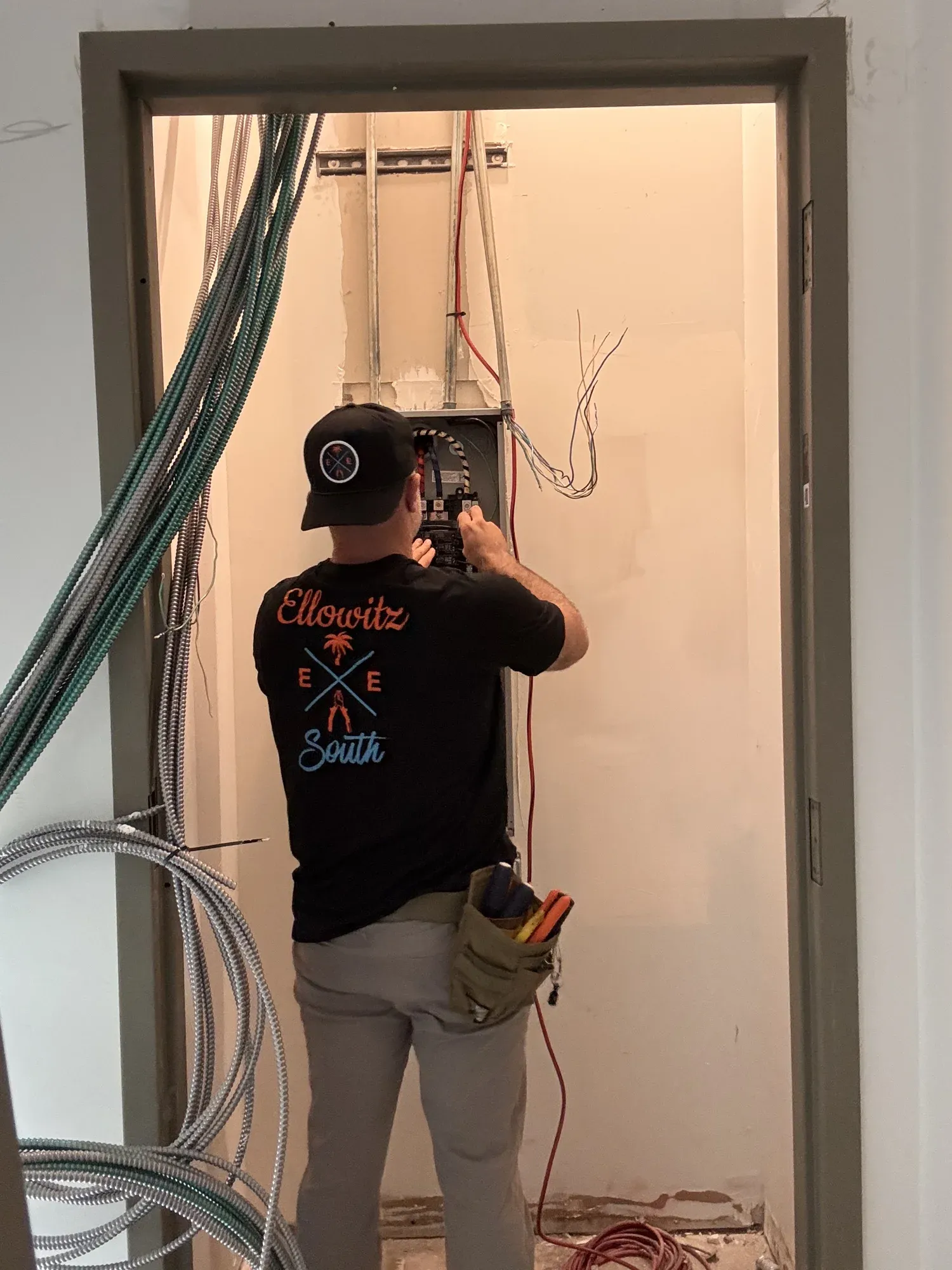 Electrician in an Ellowitz South shirt working at a panel inside an electrical closet